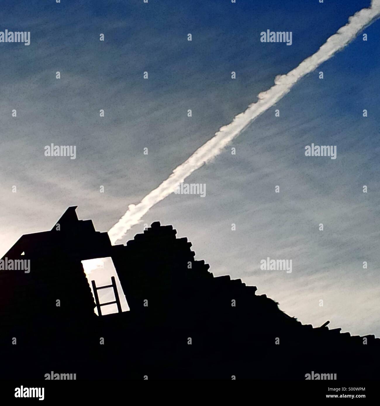 Vapour trail over a building site in London with an empty window and ladder to nowhere. Stock Photo