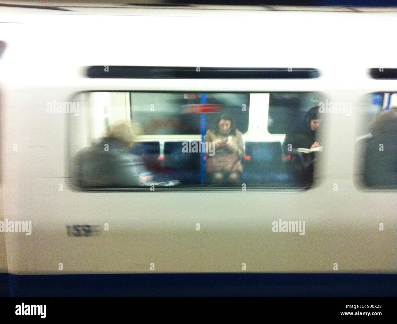 Woman using mobile phone on tube photographed through window - Smartphone Captured Stock Image