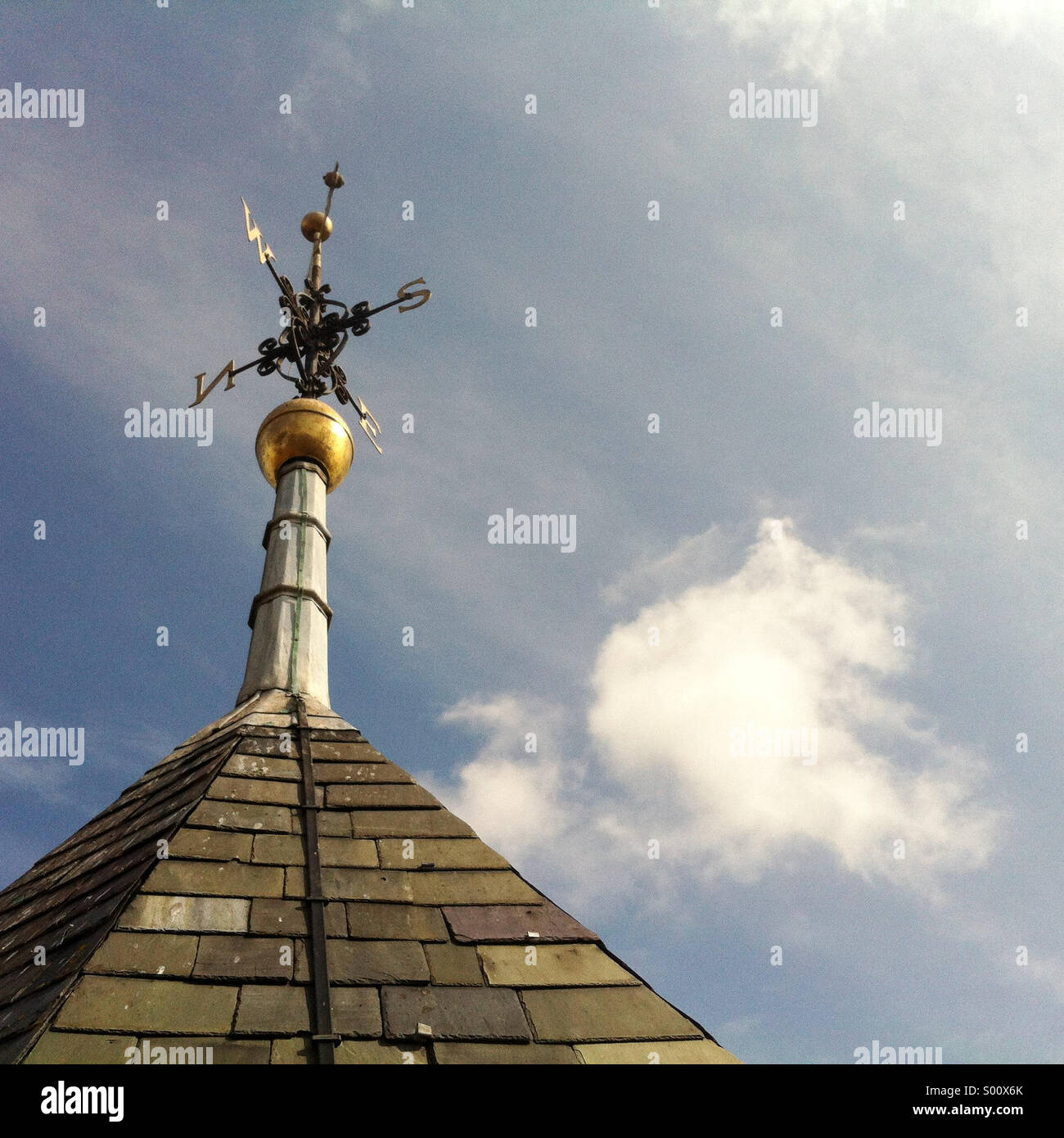 Weathervane against a blue sky with light fluffy clouds - Smartphone Captured Stock Image