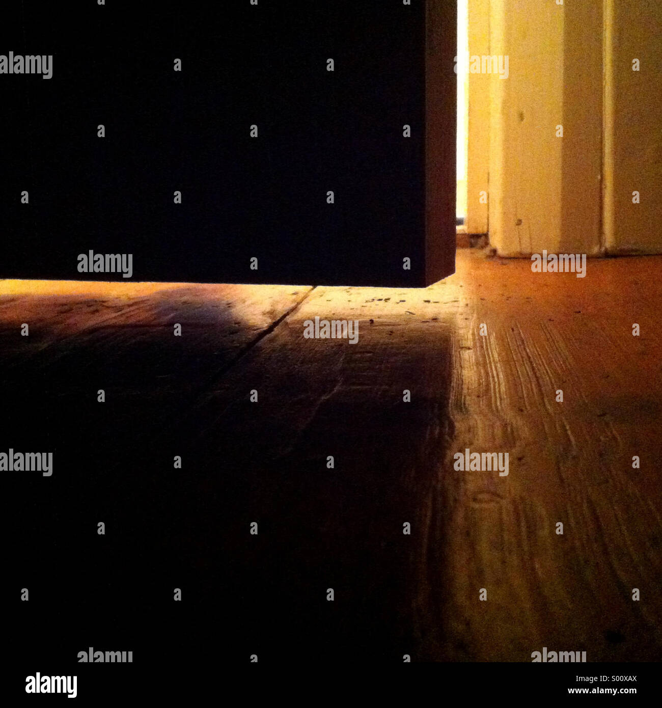 Light coming under a door just slightly ajar, spilling onto the wooden