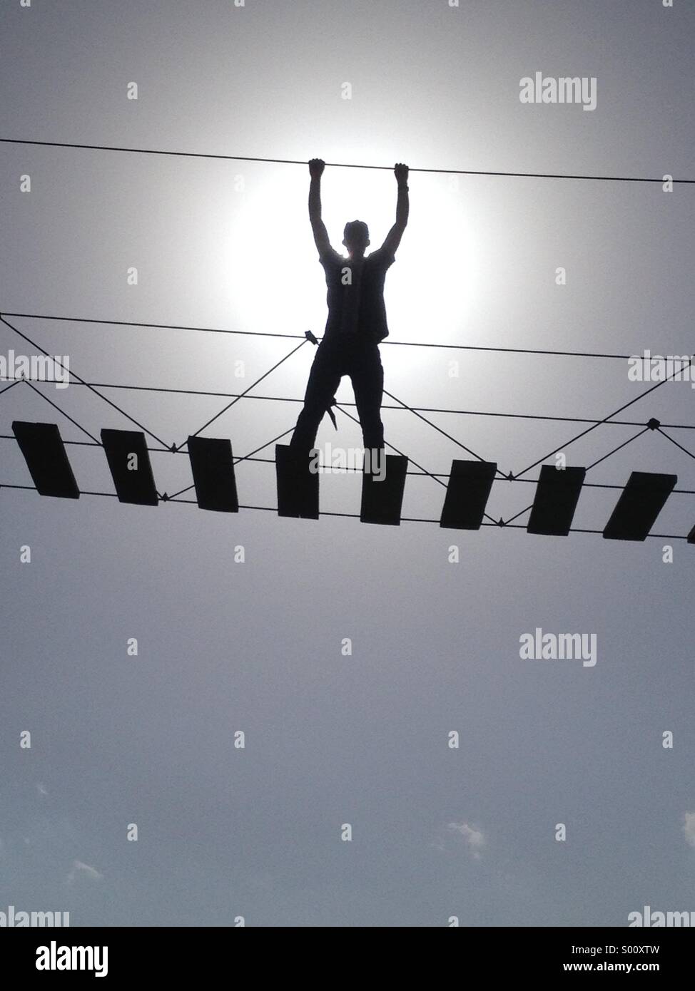 Victorious man standing on a hanging ladder, sun behind him Stock Photo