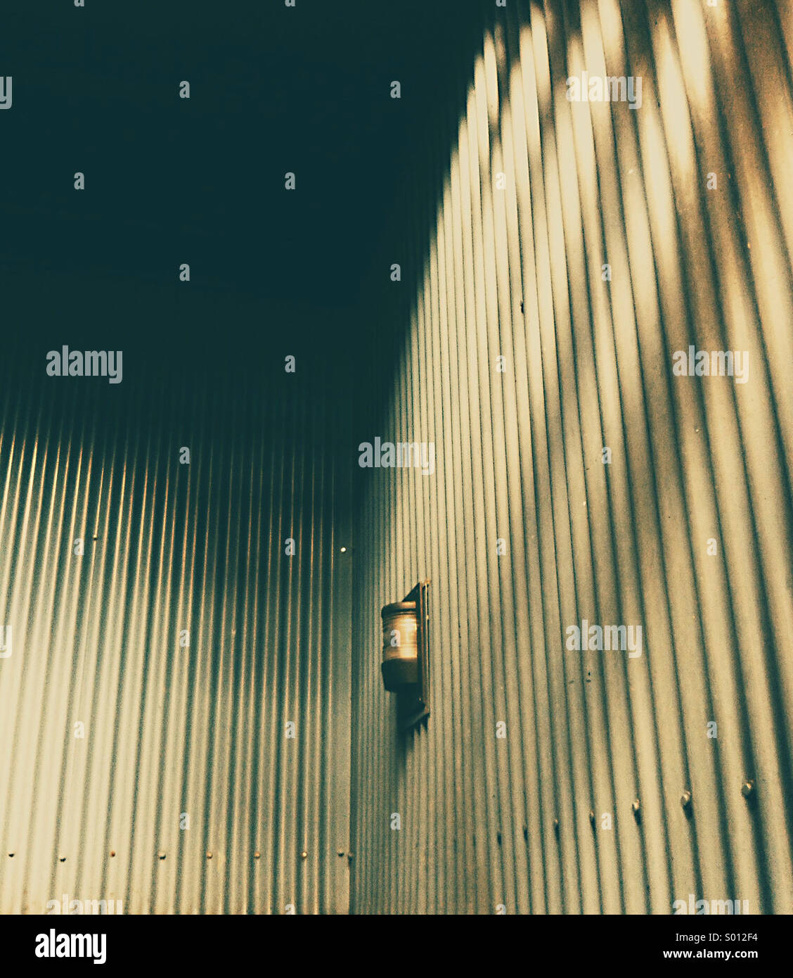 Corrugated metal clad metal stairwell with safety light and dark shadows from overhead sunlight. - Smartphone Captured Stock Image