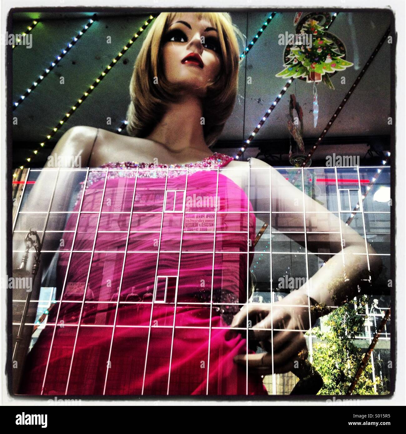 A mannequin wearing a pink dress is displayed in a fashion shop window with the reflection of a building in downtown Mexico City, Mexico - Smartphone Captured Stock Image