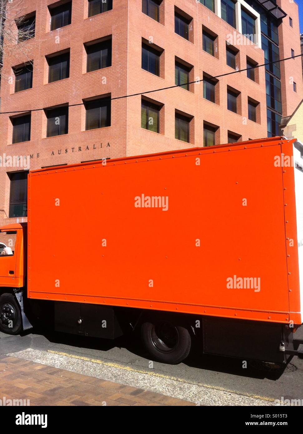 Orange truck in bright sunlight against modern building - Smartphone Captured Stock Image