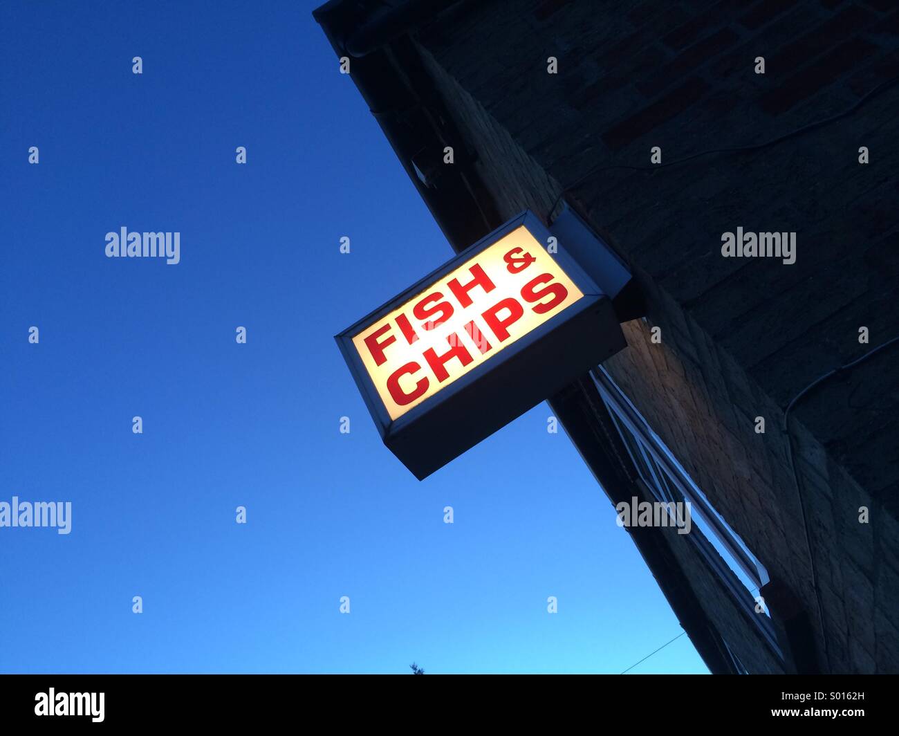 A traditional fish and chip shop sign on a wall at night in the uk. Red writing shining out against a deep blue sky - Smartphone Captured Stock Image