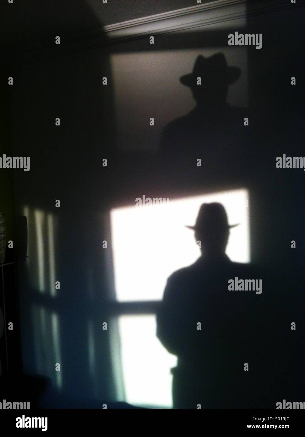 Silhouette of handsome man in hat - light from window reflected on hotel room wall and ceiling - Smartphone Captured Stock Image