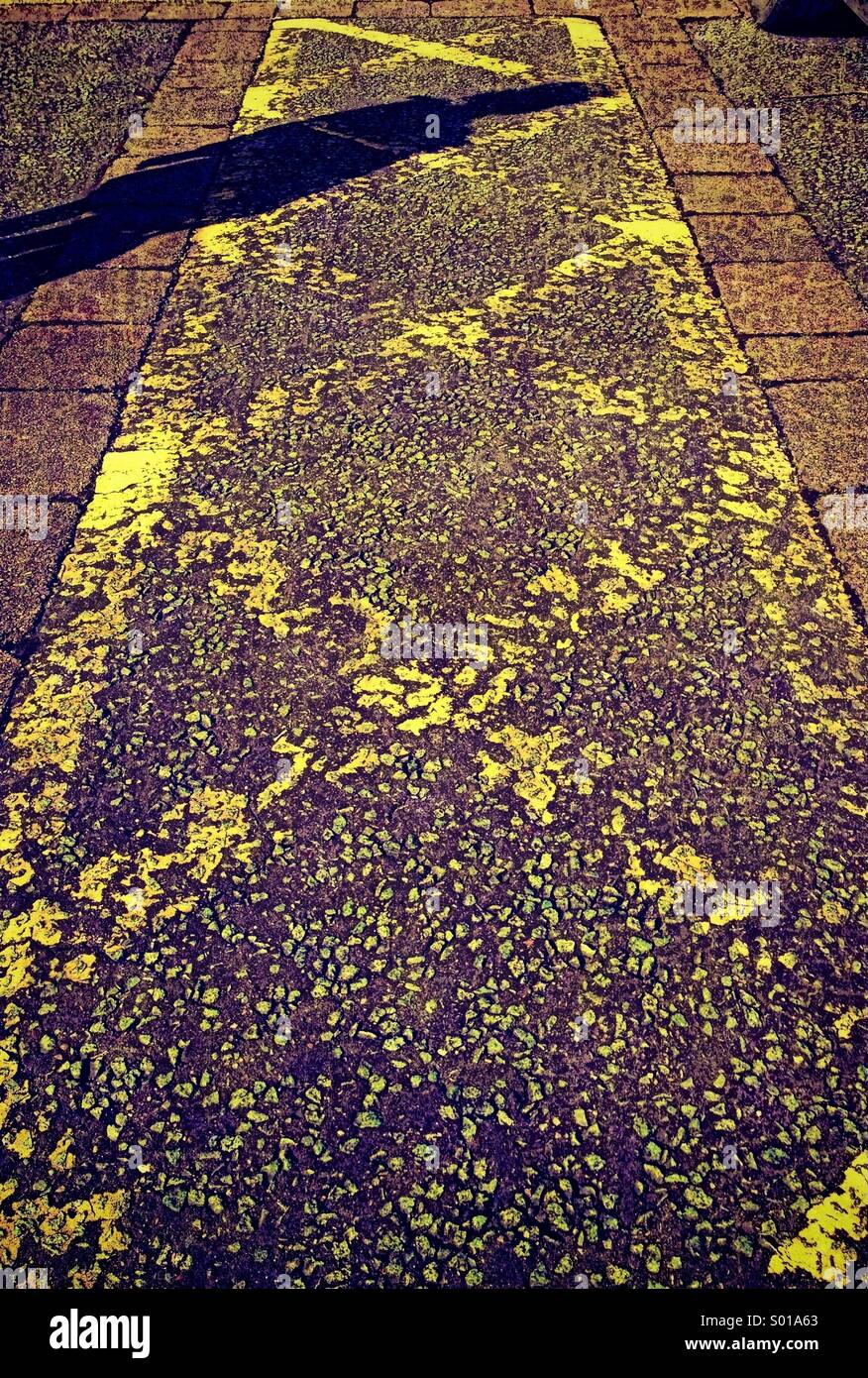 Yellow cross hatching on car park with shadow of single person Stock