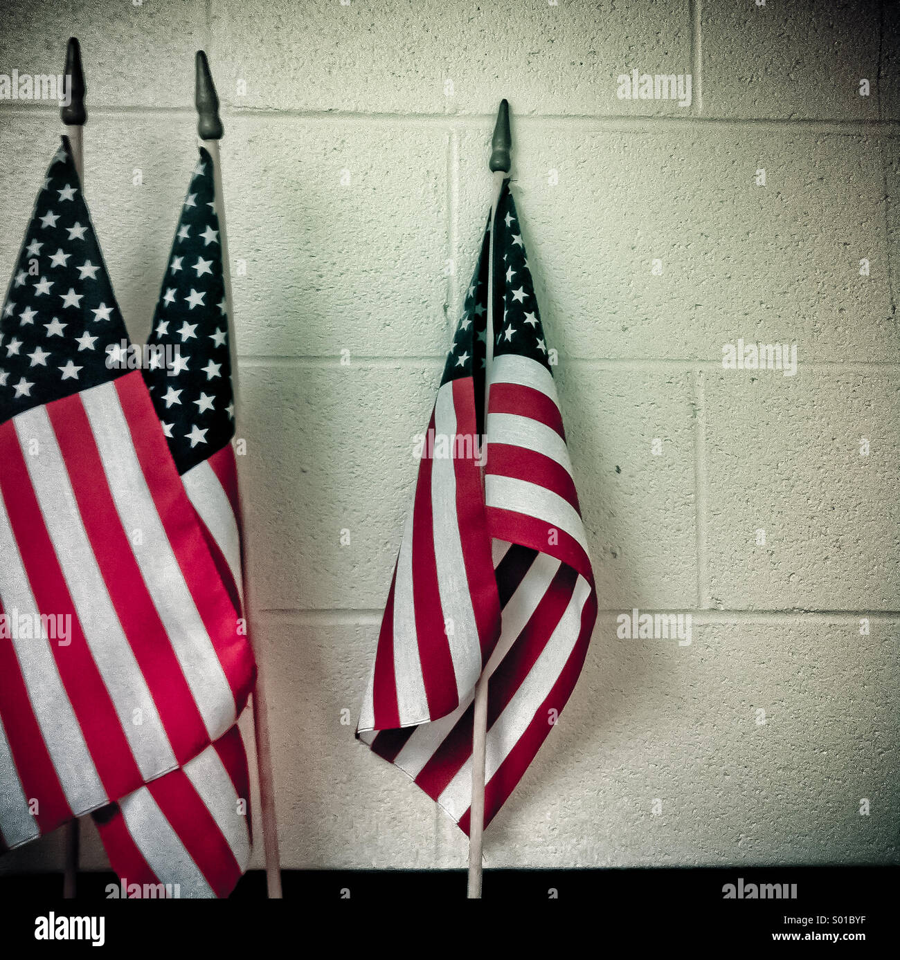 Three American flags lean against a white wall Stock Photo