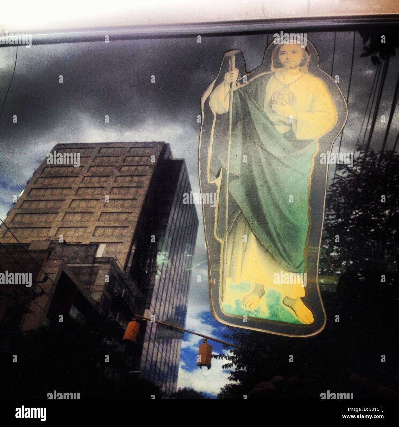 A sticker of Saint Jude Thaddeus decorates a car window reflecting building in Colonia Roma, Mexico City, Mexico - Smartphone Captured Stock Image