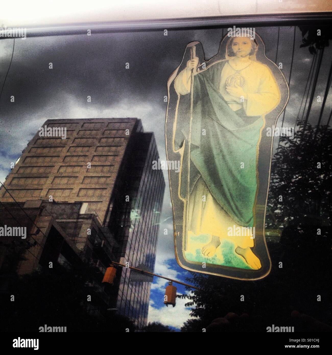 A sticker of Saint Jude Thaddeus decorates a car window reflecting building in Colonia Roma, Mexico City, Mexico Stock Photo