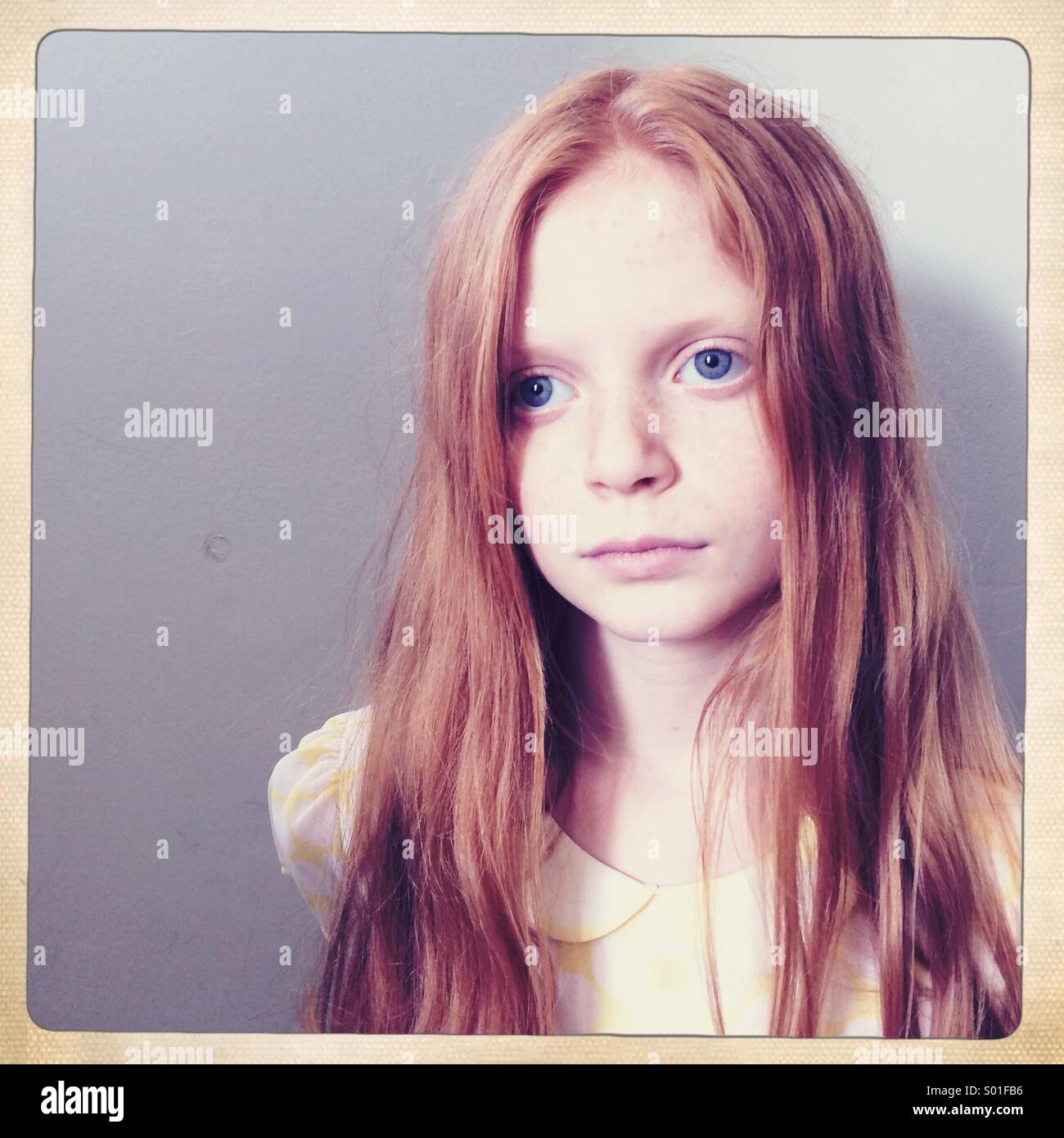 Red haired girl stares blankly off camera with a plain grey background Stock Photo