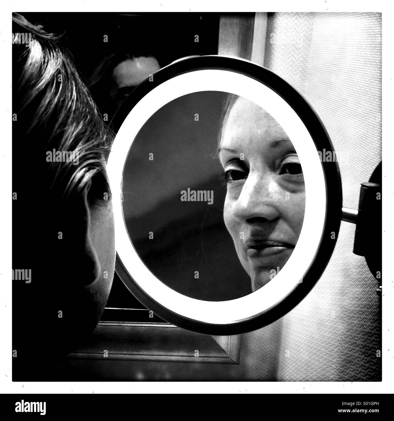 A woman looks into a vanity mirror Stock Photo - Alamy