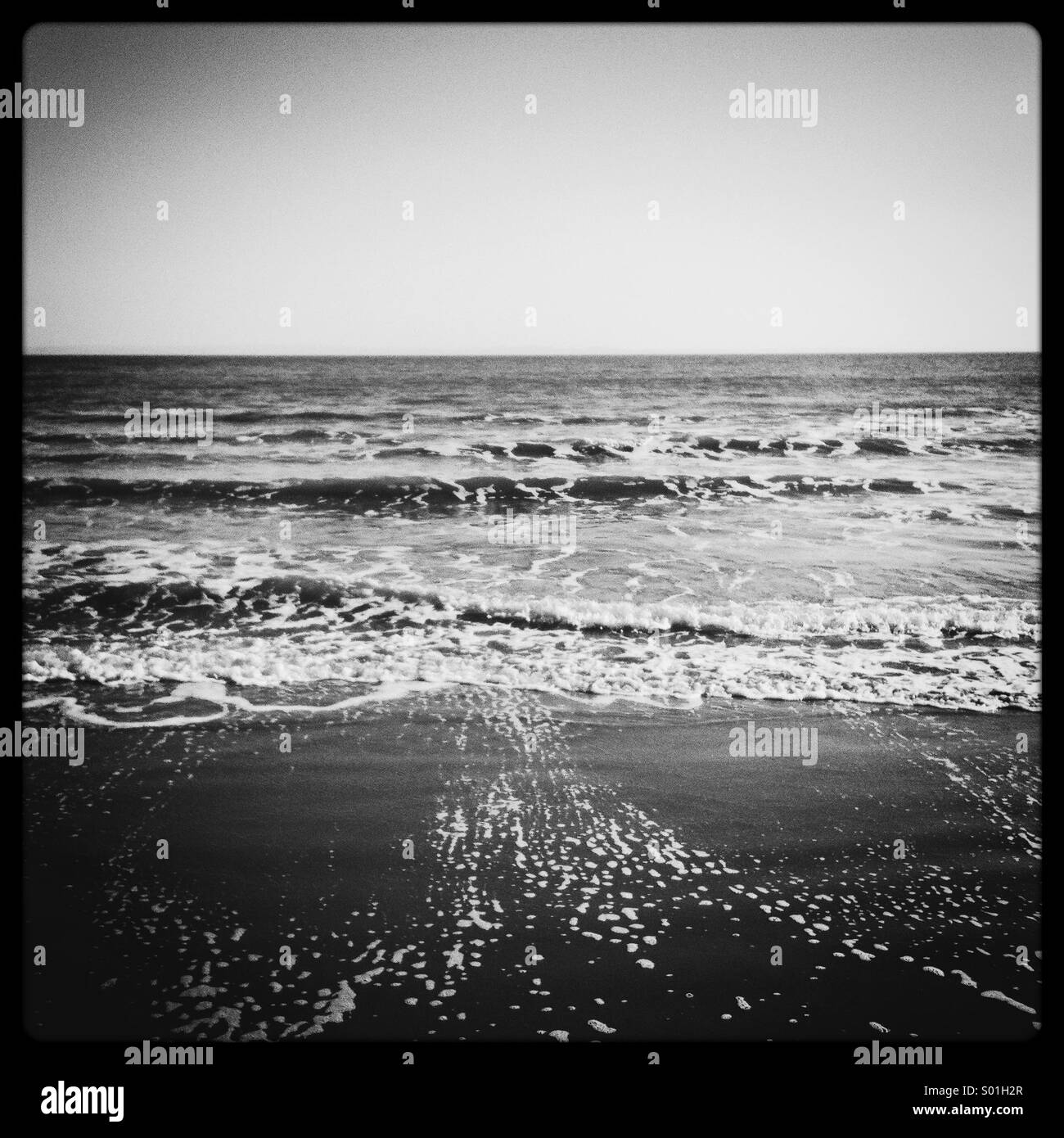 Black and white photograph of the shore as waves pull back from the sand Stock Photo