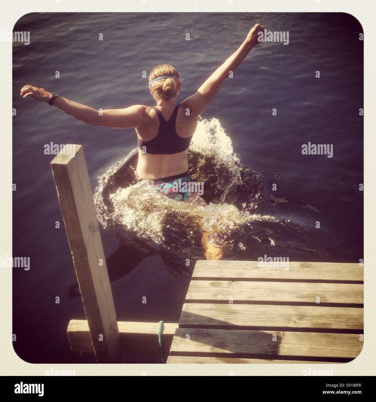 A woman jumping off a pier into a lake Stock Photo