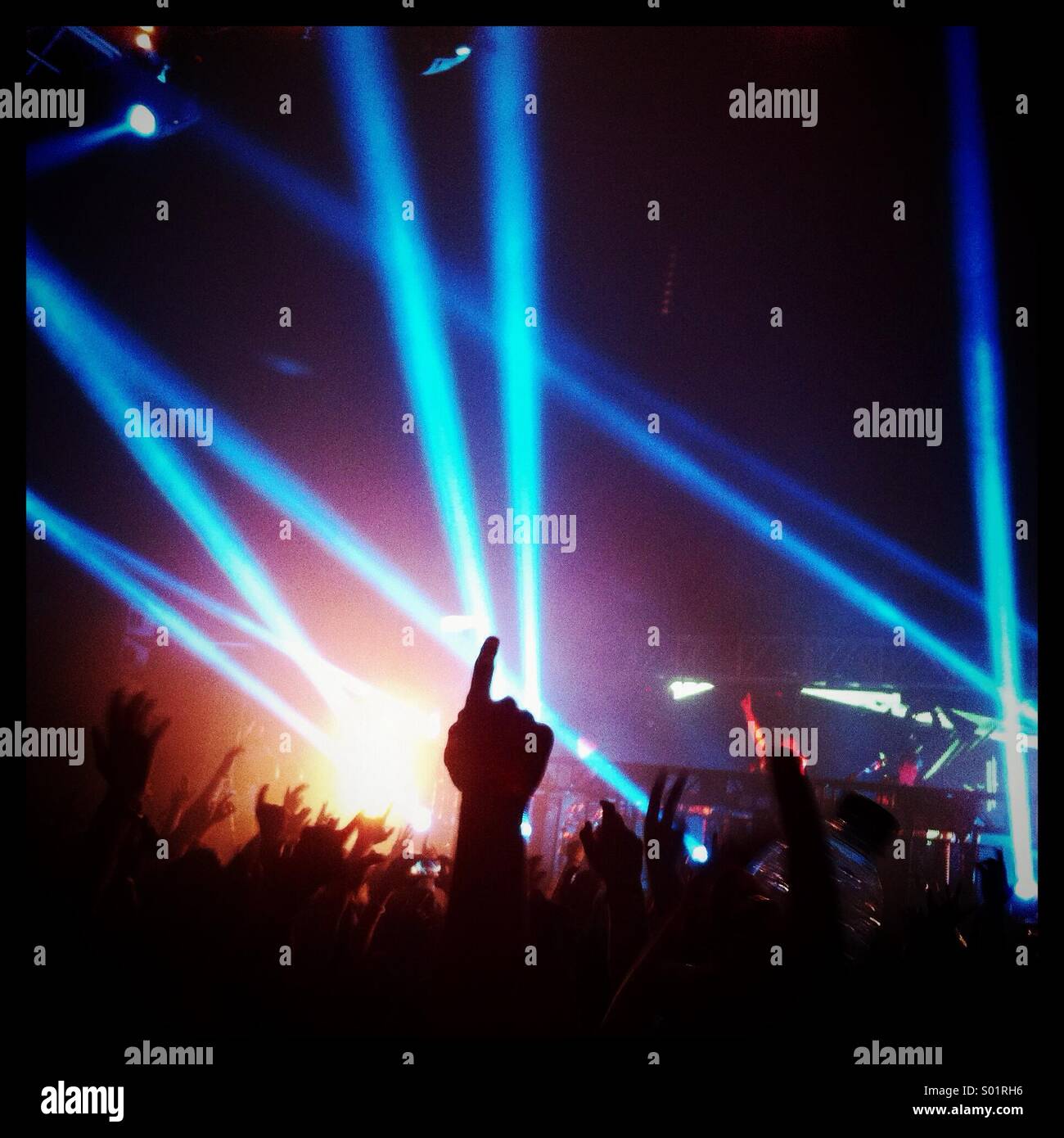View from the pit at Reading Festival, with the silhouette of a pointing finger centred against a background of blue lights coming from the stage. Stock Photo