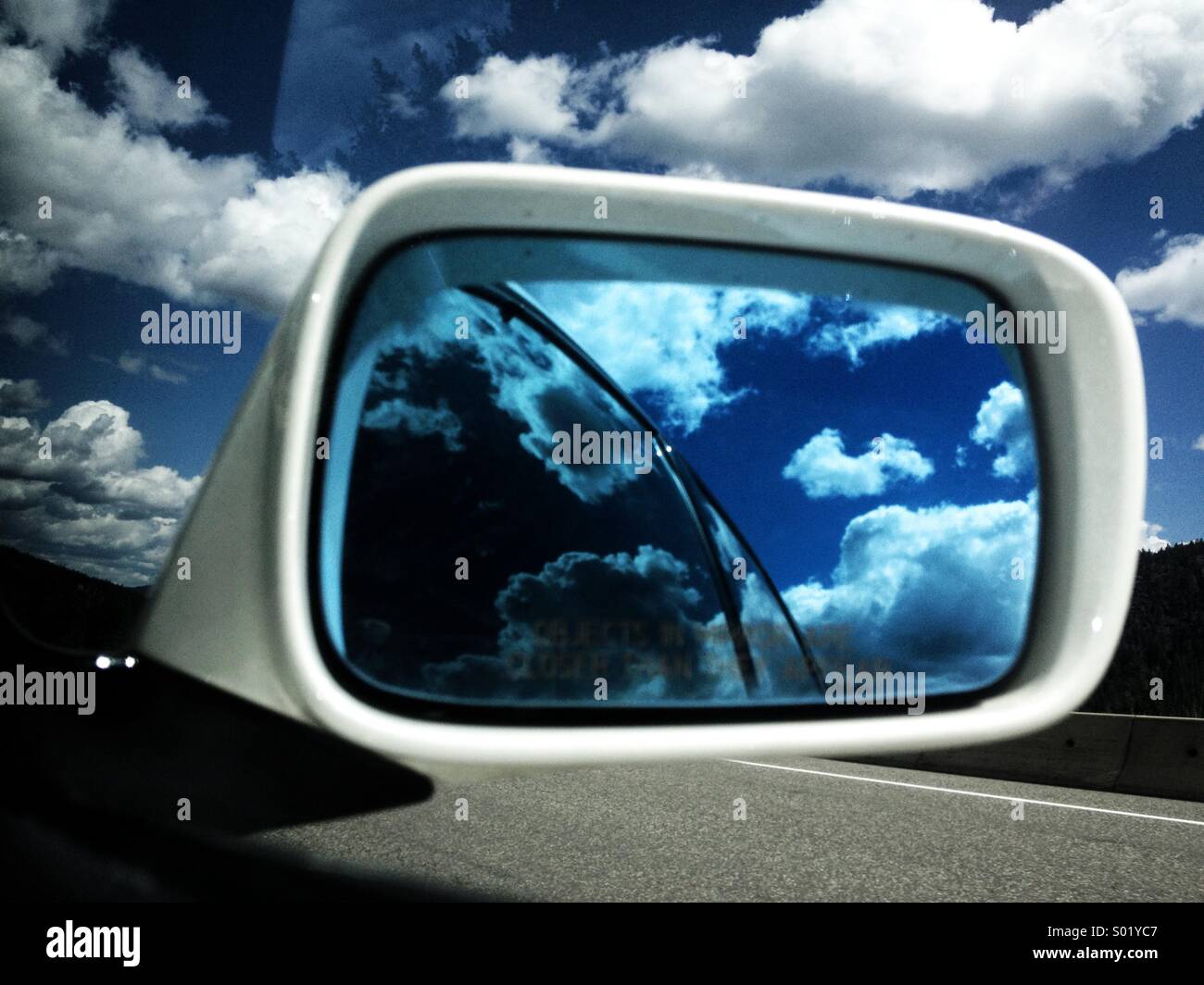 Road trip reflections. White clouds and blue sky reflecting in side mirror of car. - Smartphone Captured Stock Image