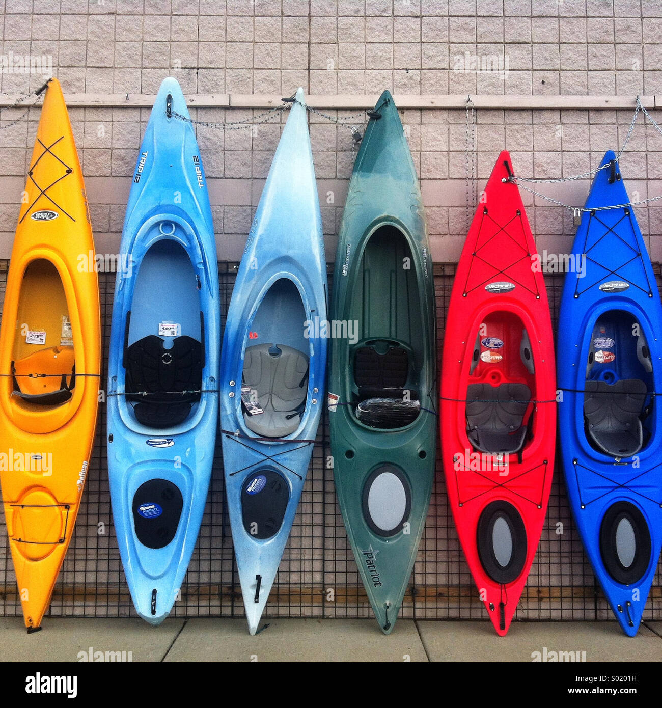 A row of colorful kayaks propped against a wall Stock Photo