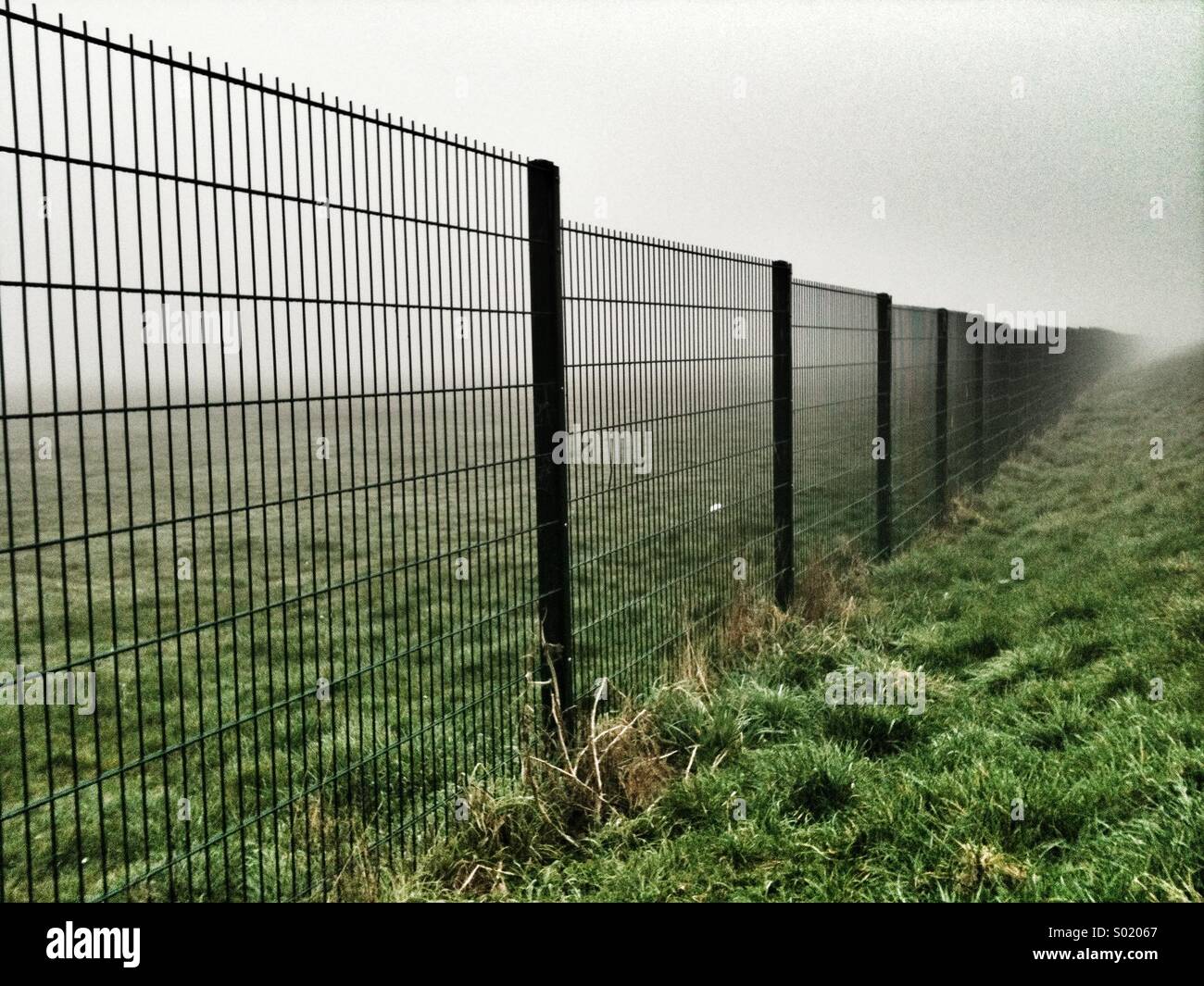 Metal fence vanishes into distant fog. - Smartphone Captured Stock Image