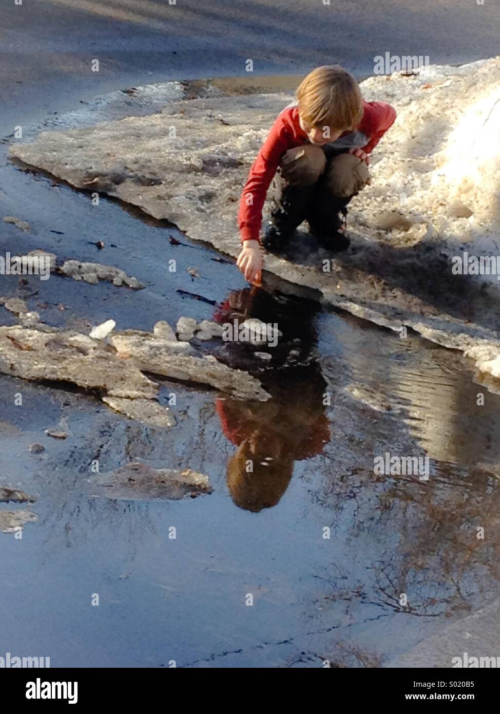 7 year old boy plays in the spring meltwater Stock Photo