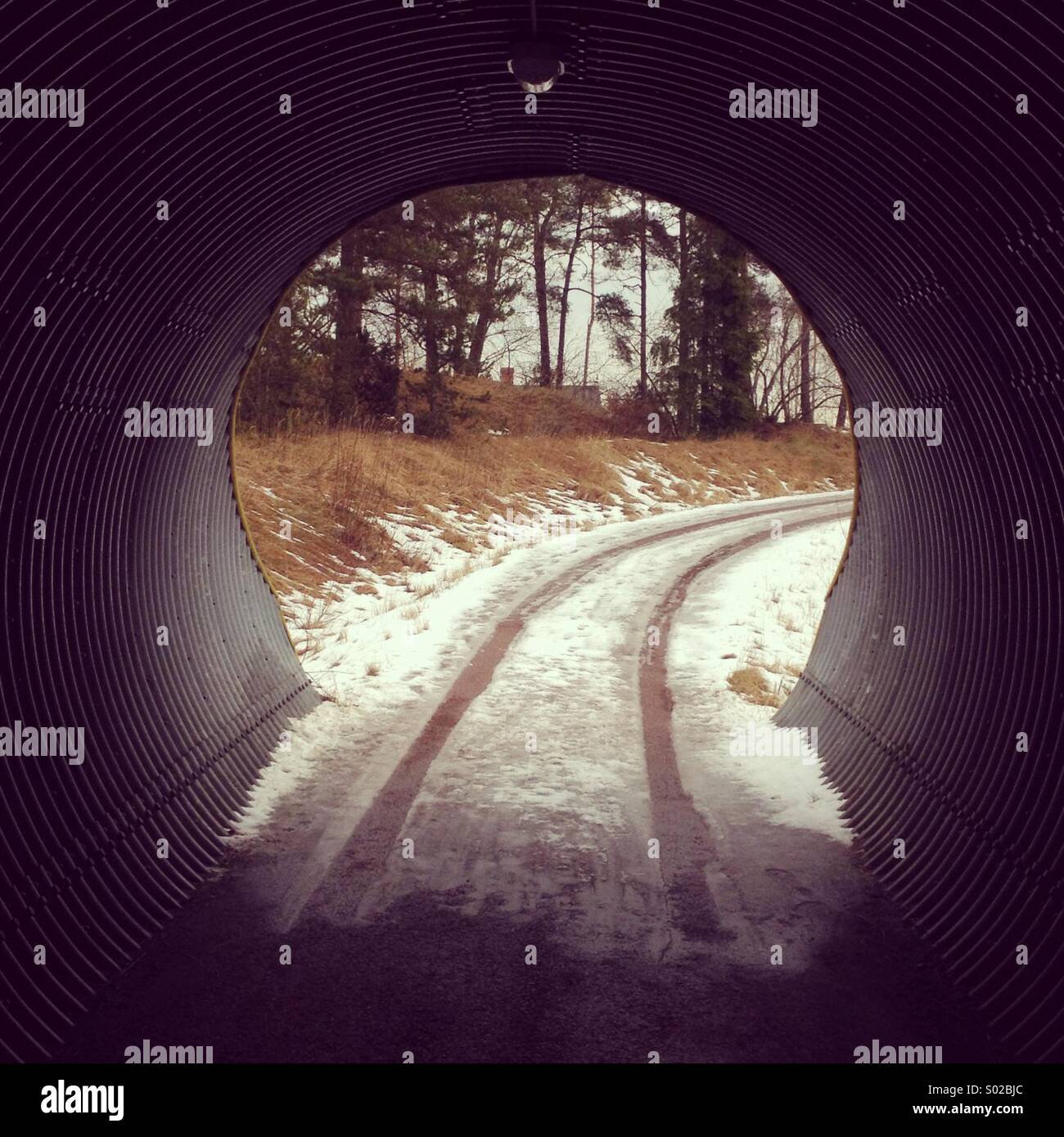 Ice and snow covered road leading out of a keyhole shaped bicycle tunnel - Smartphone Captured Stock Image