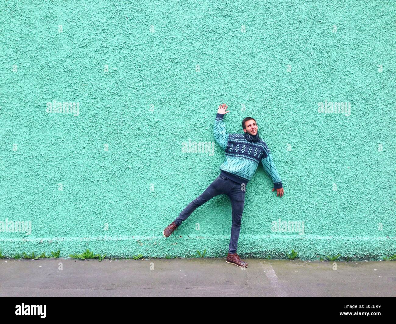 Man simulating that he's been stuck on a green wall Stock Photo