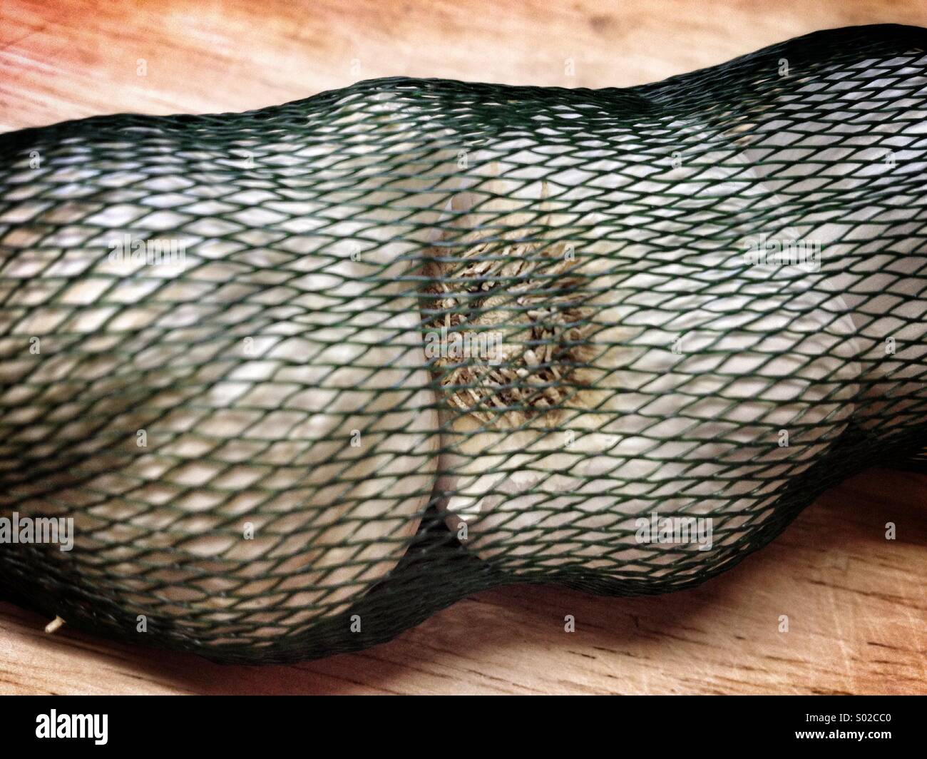 Cloves of garlic in a net on a chopping board - Smartphone Captured Stock Image