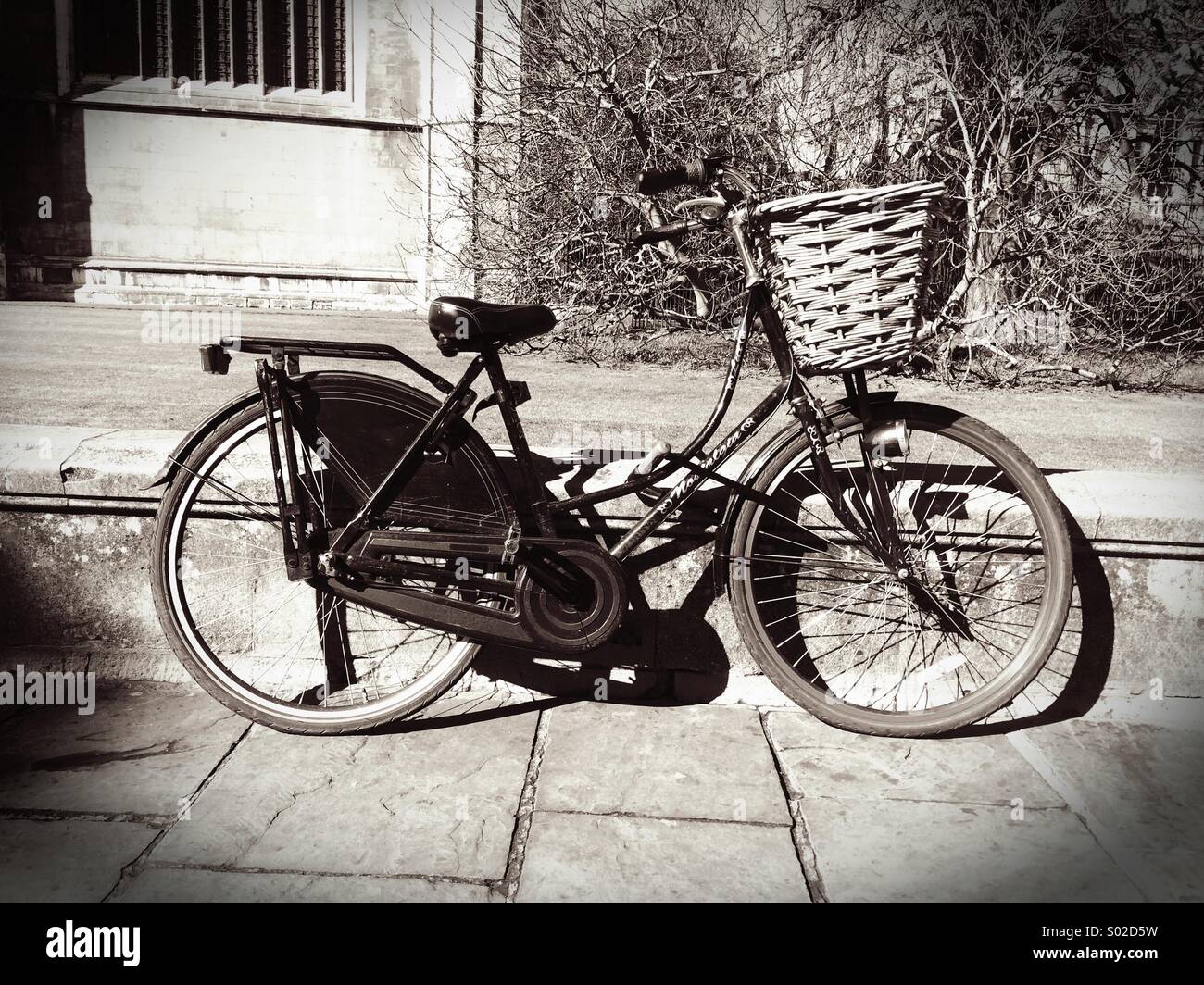 A traditional pedal cycle with basket leaning against a wall in Cambridge UK  with vintage black and white filter - Smartphone Captured Stock Image