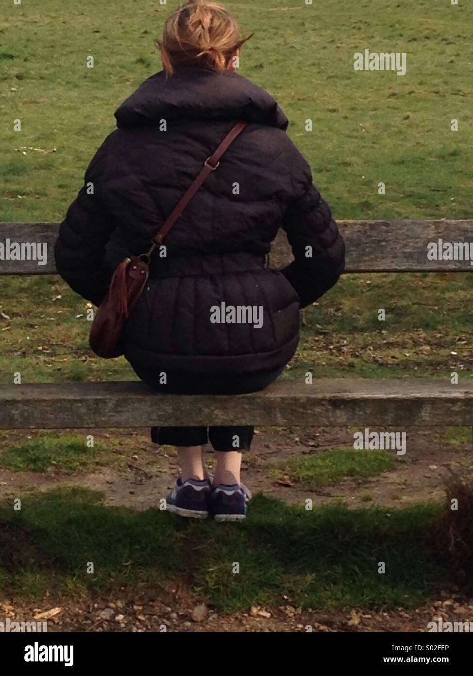 Young woman's back view  in brown Coat on wooden bench - Smartphone Captured Stock Image