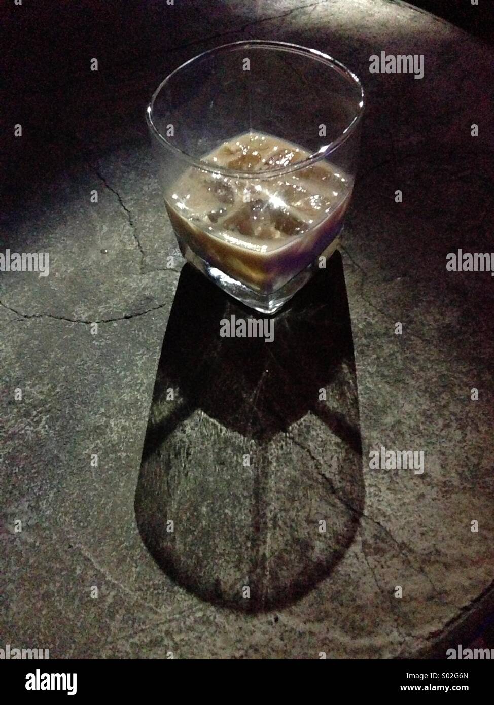 Glass of Baileys liqueur on ice on a stone table with light and shadow. Alcoholic drink. Stock Photo