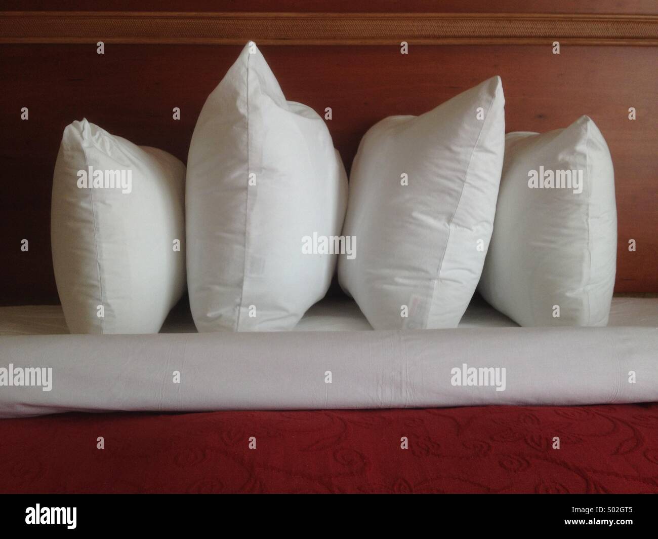 Hospitality in bed: Four pillows by wooden baseboard in window light Stock Photo