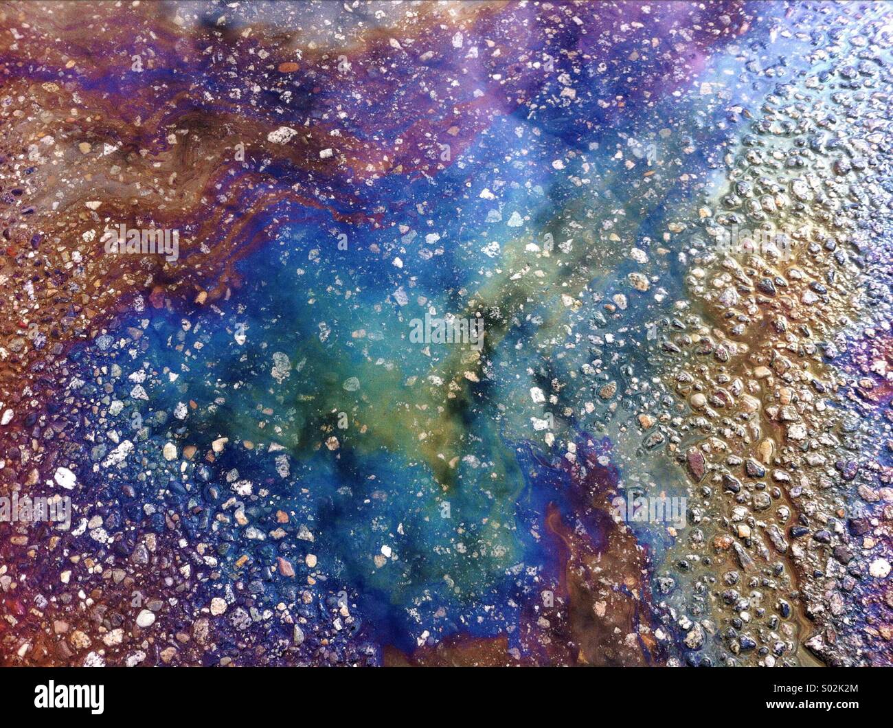 Iridescent rainbow coloured oil slick, leaked from a parked car on wet asphalt. - Smartphone Captured Stock Image