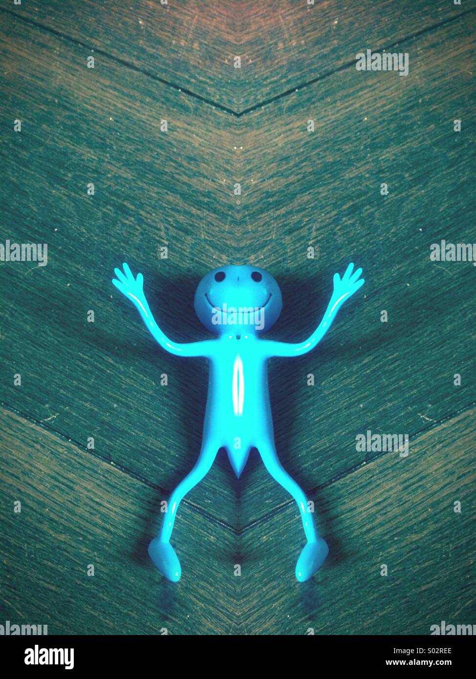 Smiley mirrored blue alien toy lying on a wooden floor Stock Photo