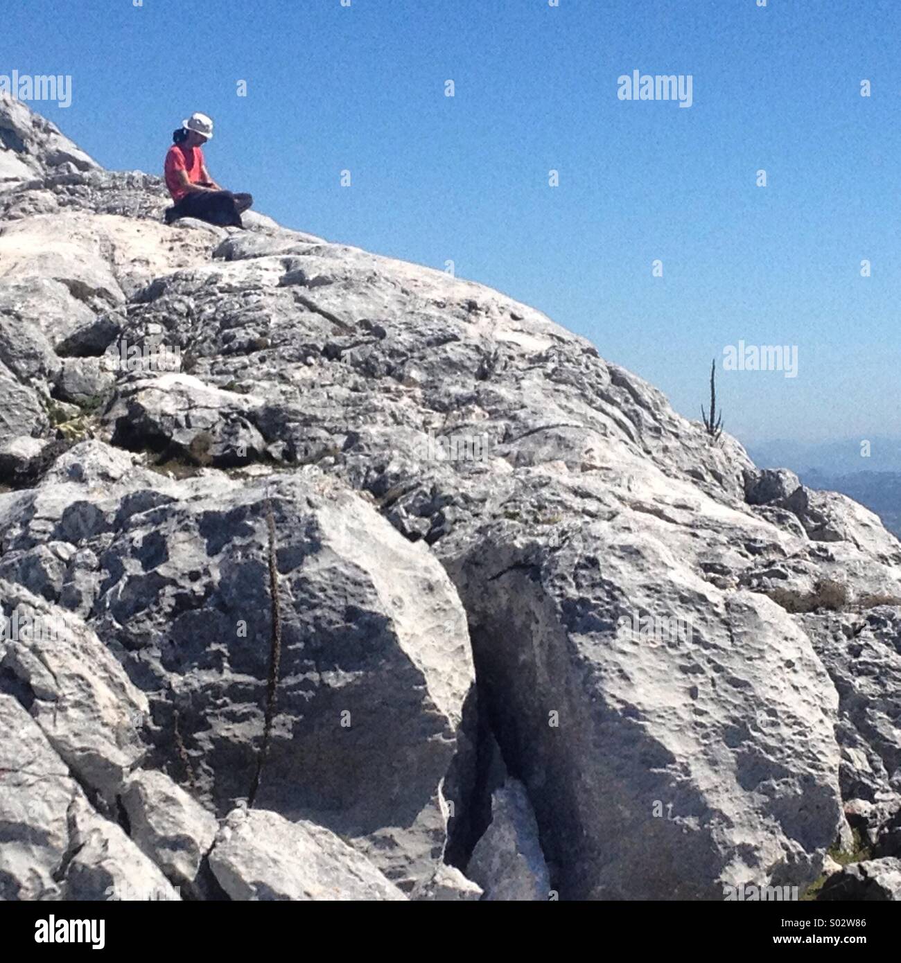 A tourist sits on top of Simancon mountain peak in the Parque Natural Sierra de Grazalema Natural Park, Grazalema, Cadiz province, Andalusia, Spain - Smartphone Captured Stock Image