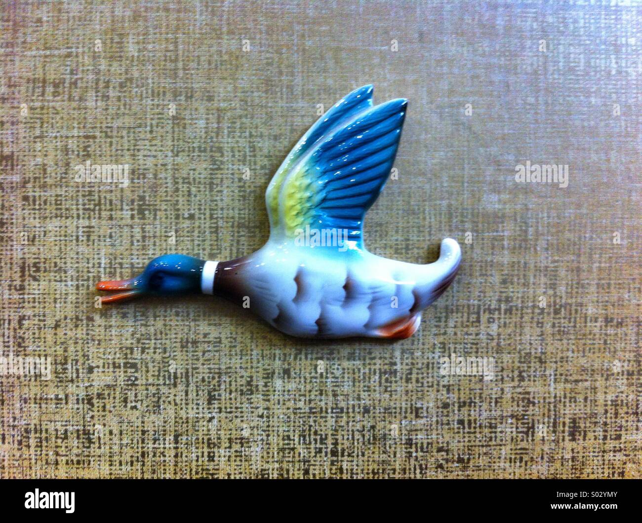 Decorative flying duck figurine crafted with intricate detailing and vibrant colors displayed against a textured background - Smartphone Captured Stock Image