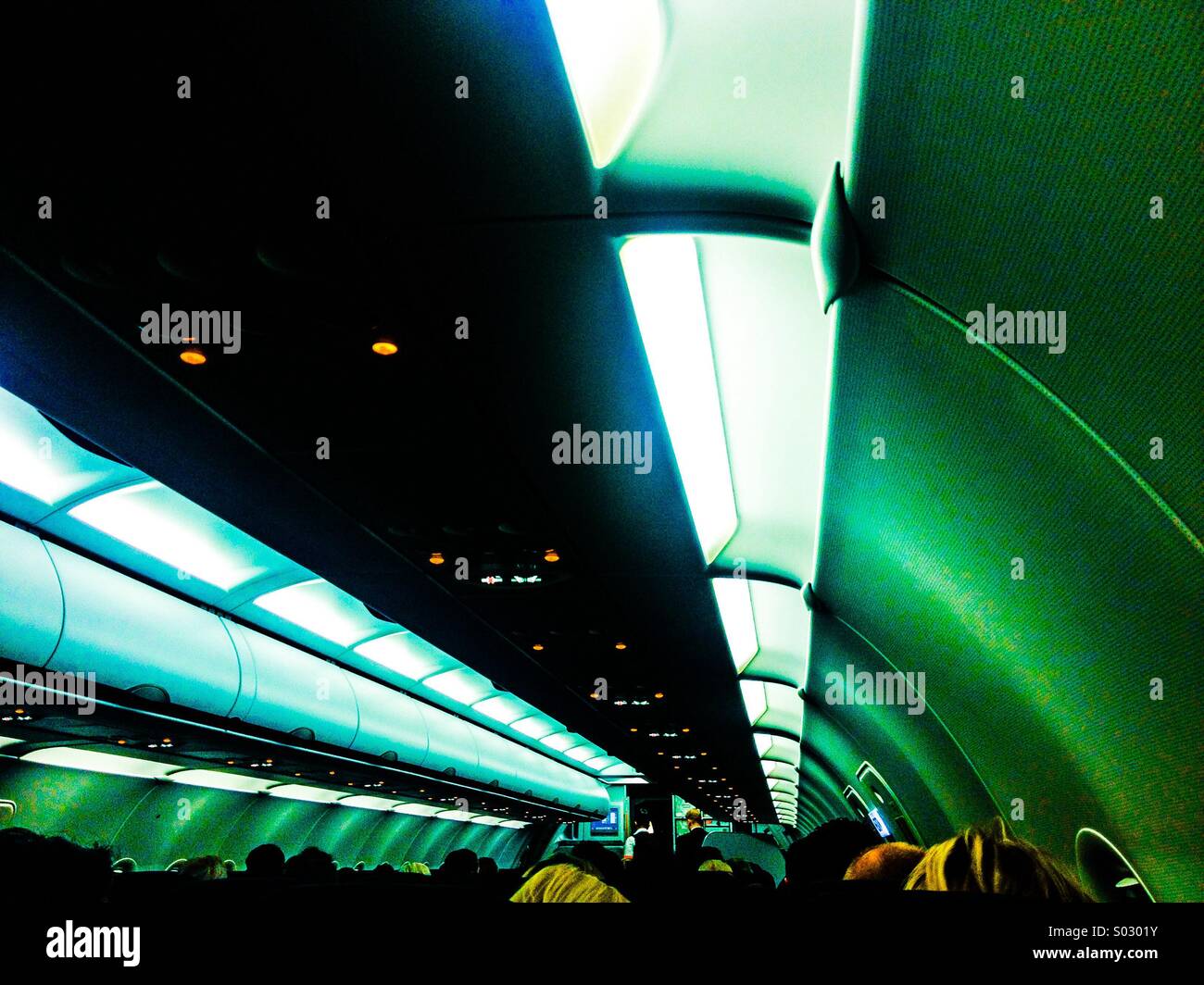 Inside of plane looking down over the heads of passengers to steward Stock Photo