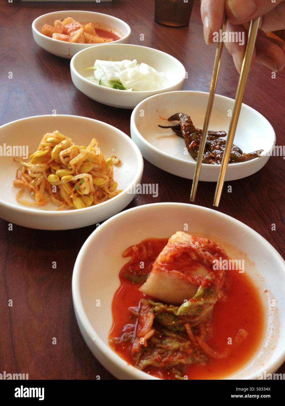 Korean appetizers in dishes with hand holding chopsticks Stock Photo