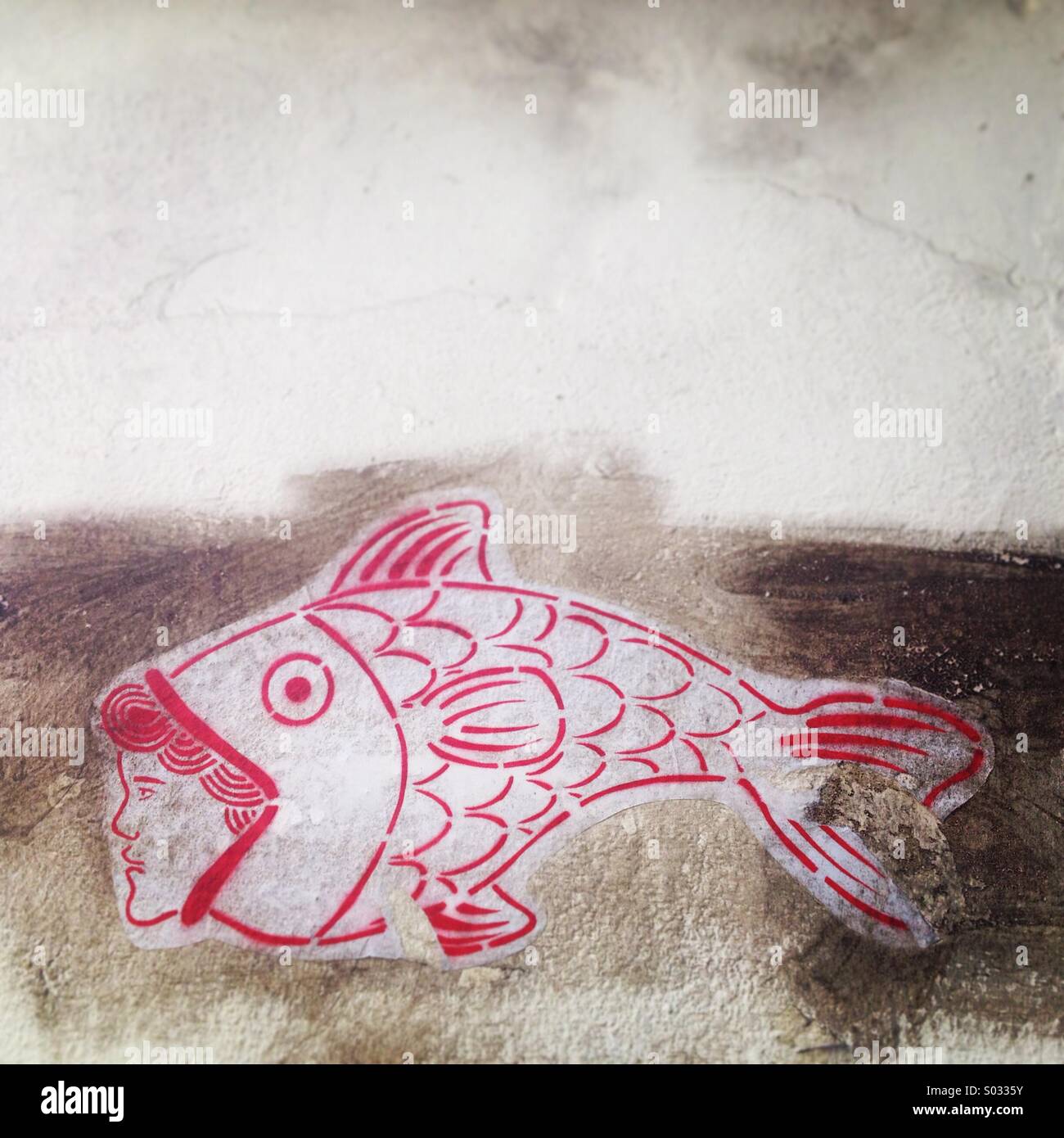 A red sticker of a fish eating a man decorates a wall in Caceres, Extremadura, Spain - Smartphone Captured Stock Image