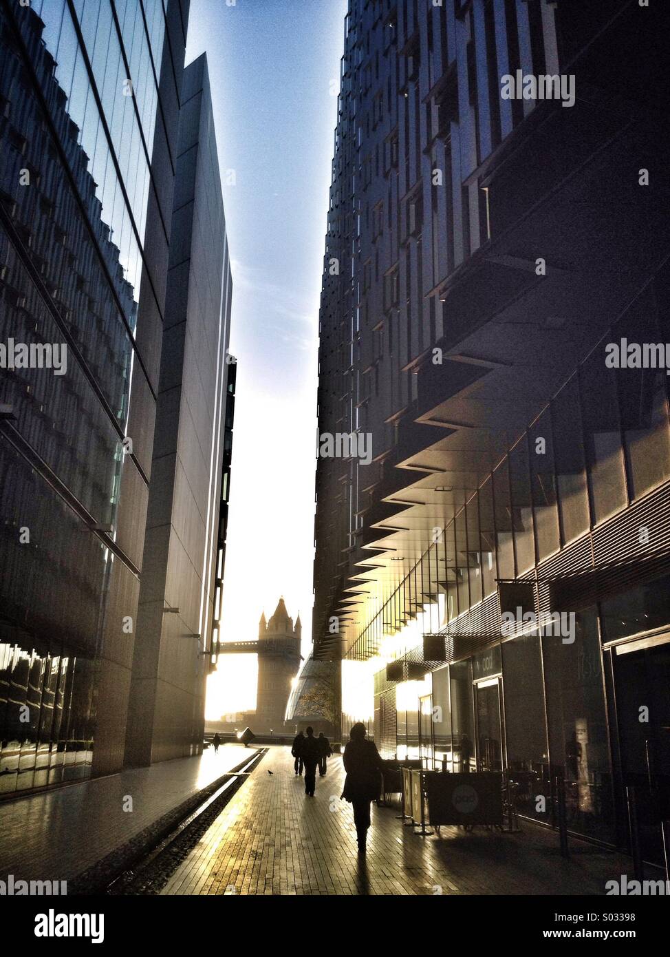Commuters make their way along More London towards Tower Bridge which is framed between office buildings - Smartphone Captured Stock Image