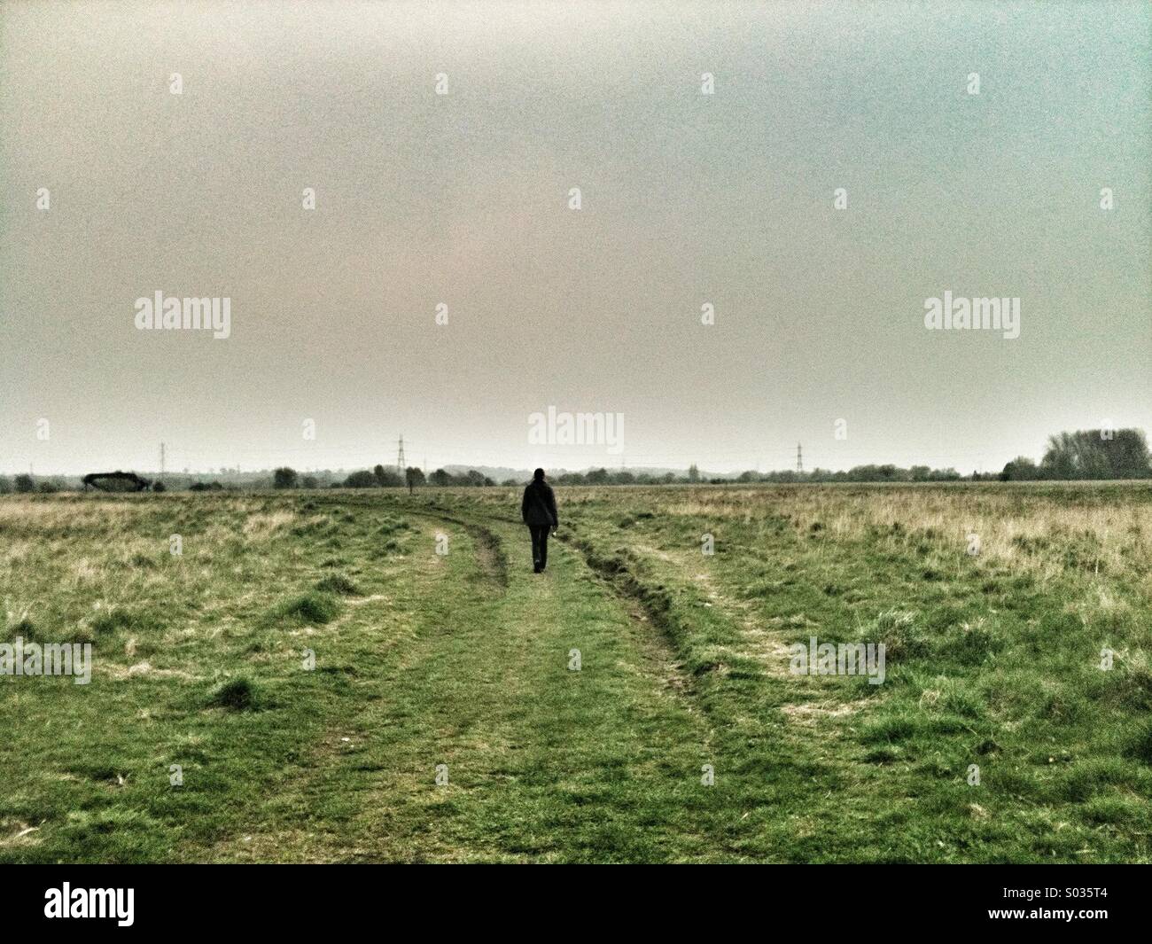 Single person in silhouette walks along  grassy path. - Smartphone Captured Stock Image
