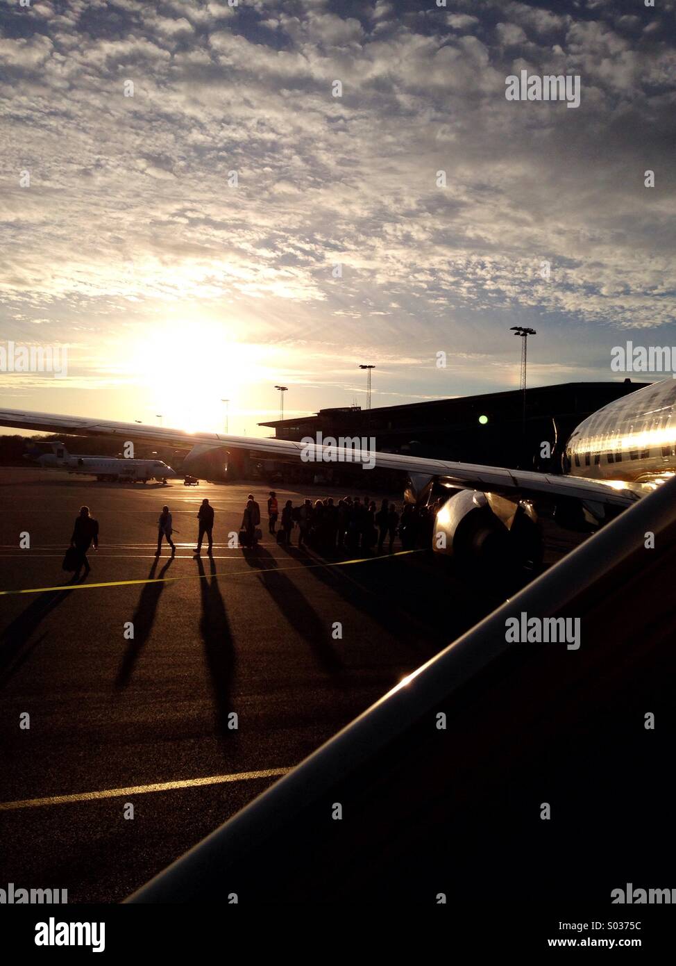 About to board in a Ryan Air airplane, in Billund, in the Jutland peninsula, Denmark, with the sunset in the background and the silhouettes of passengers, for a flight from Billund to Faro, Portugal - Smartphone Captured Stock Image