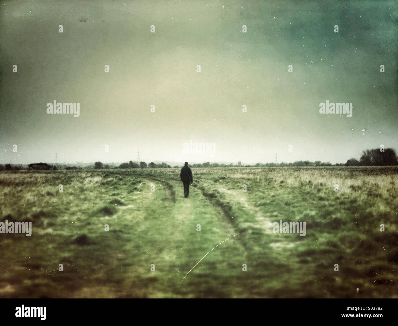 Single person  walks along along a grassy path. Grunge effect filter applied. - Smartphone Captured Stock Image