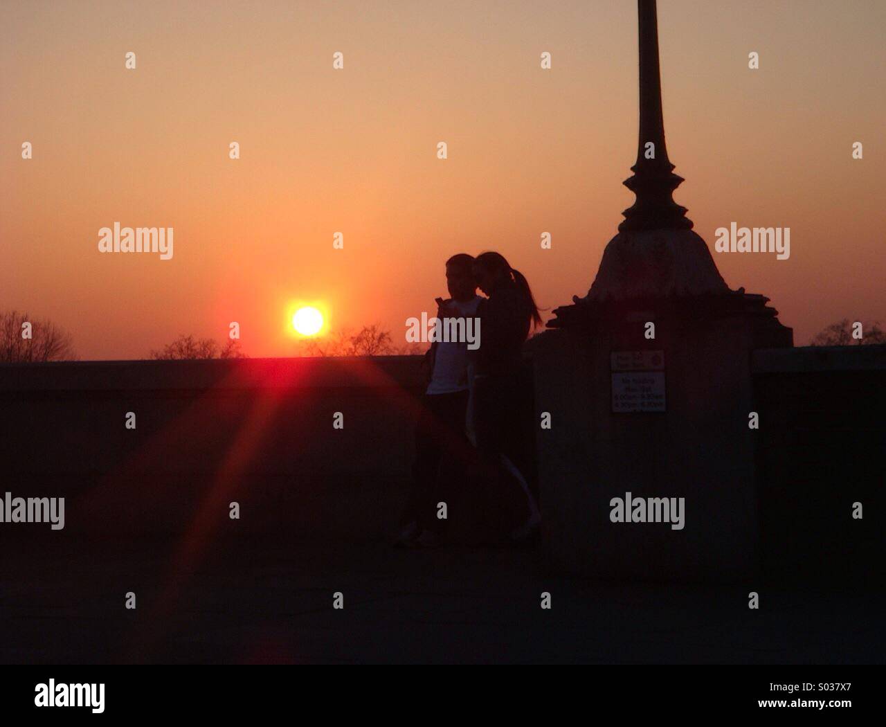Lovers at sunset on Putney bridge in London.watching the setting sun by one of the Victorian gas lamps.. - Smartphone Captured Stock Image