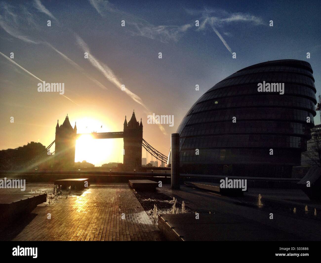The sun rises behind Tower Bridge in London, with City Hall on the right. - Smartphone Captured Stock Image