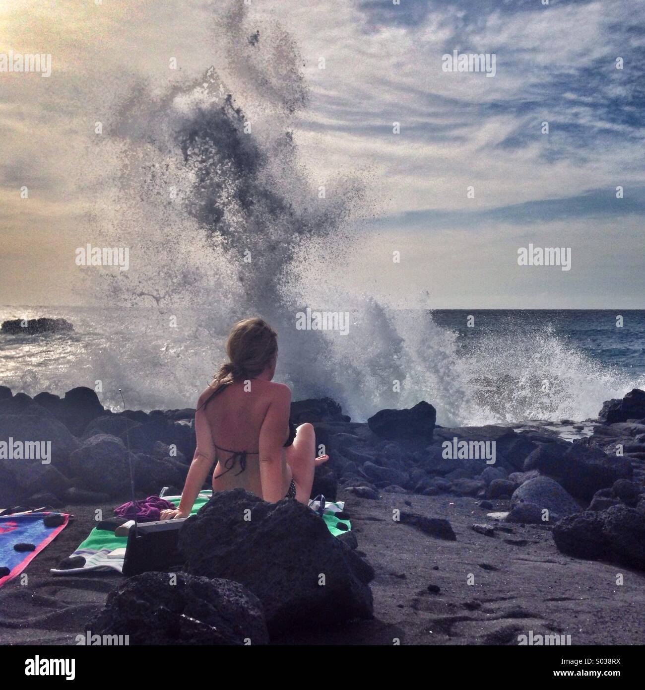 Girl on a black sand beach in Hawaii watching waves break on rocks Stock Photo