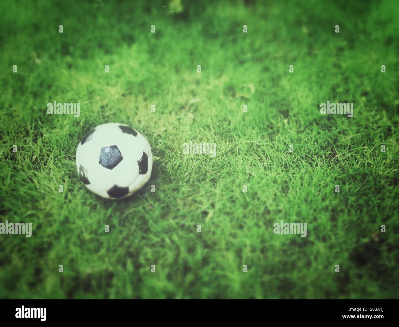 Old football, deflated on grass. Grunge and tilt-shift effects applied. - Smartphone Captured Stock Image