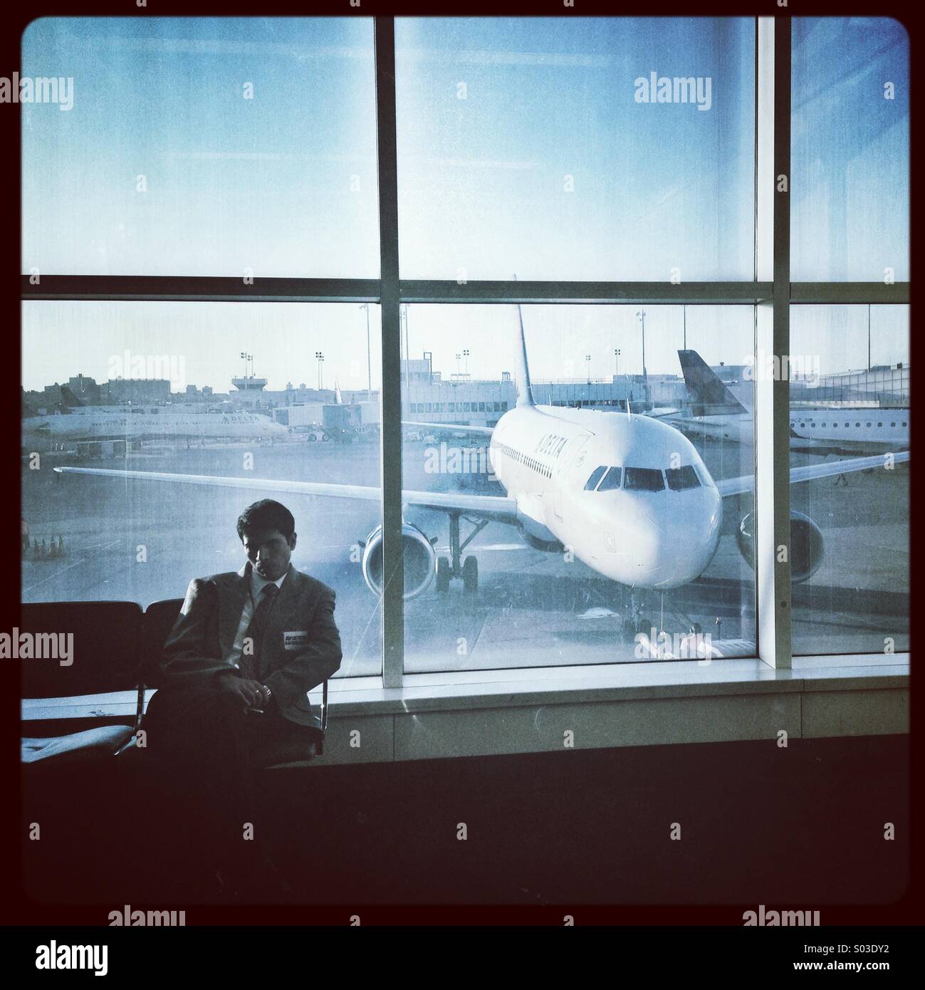 Man sitting in airport terminal with jet aircraft in window behind - Smartphone Captured Stock Image