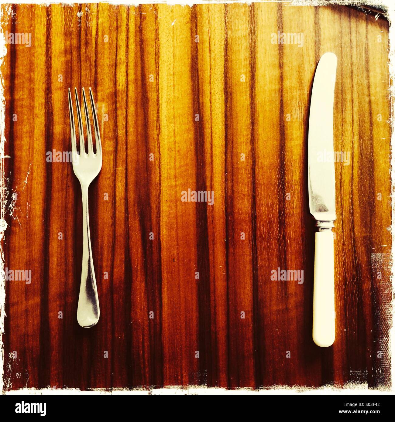 Knife and fork on highly polished stylish wood grain retro 1960's dining table - Smartphone Captured Stock Image