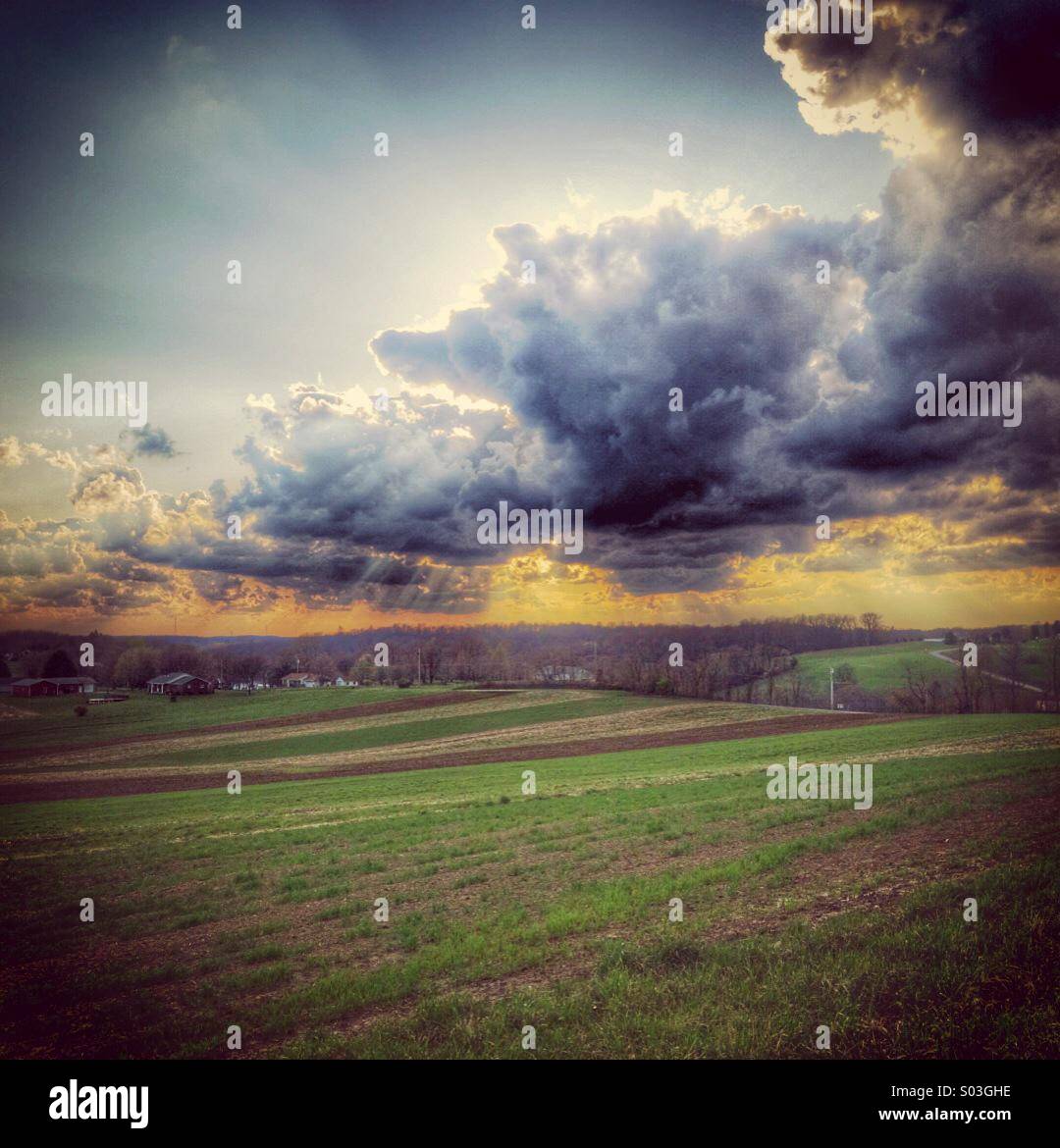 A dramatic cloudy sky over a field at sunset Stock Photo