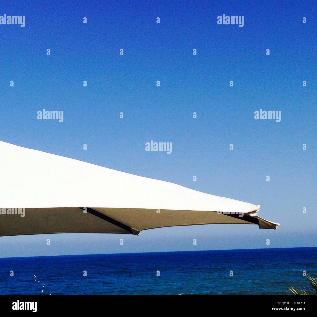 Sun umbrella white facing the blue sea under a blue sky creating an abstract image. - Smartphone Captured Stock Image