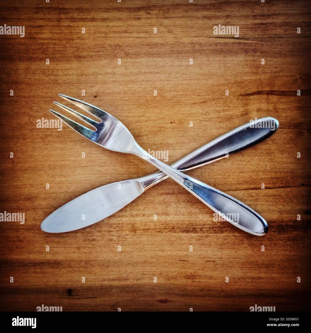 Crossed knife and fork on a wooden table - Smartphone Captured Stock Image